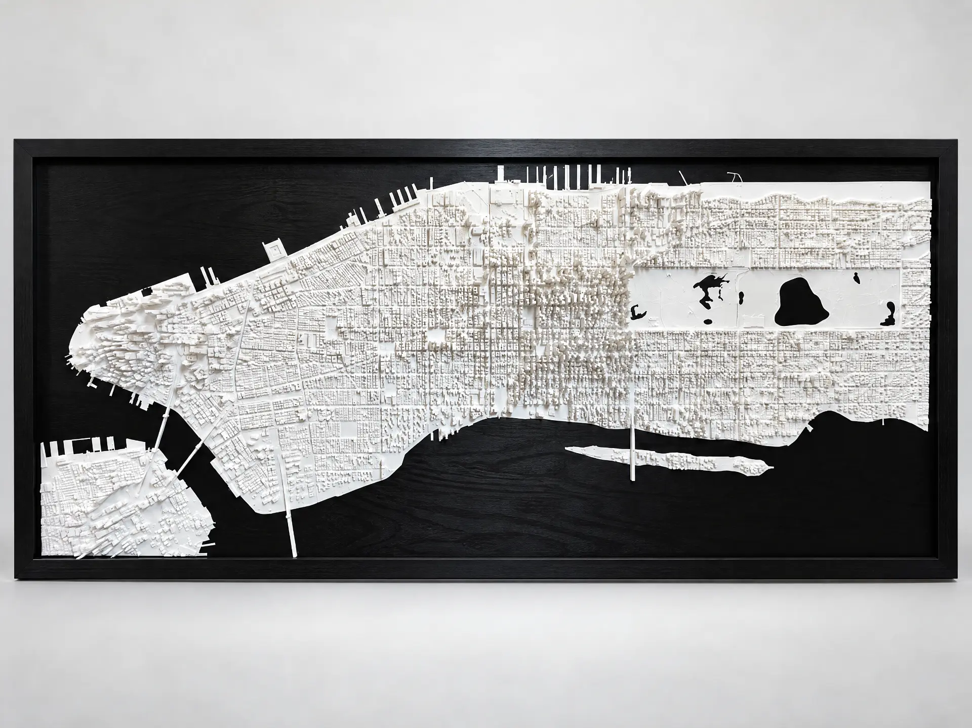 Framed 3D-printed relief map of Manhattan printed in white and mounted in a black frame, on a light grey studio background