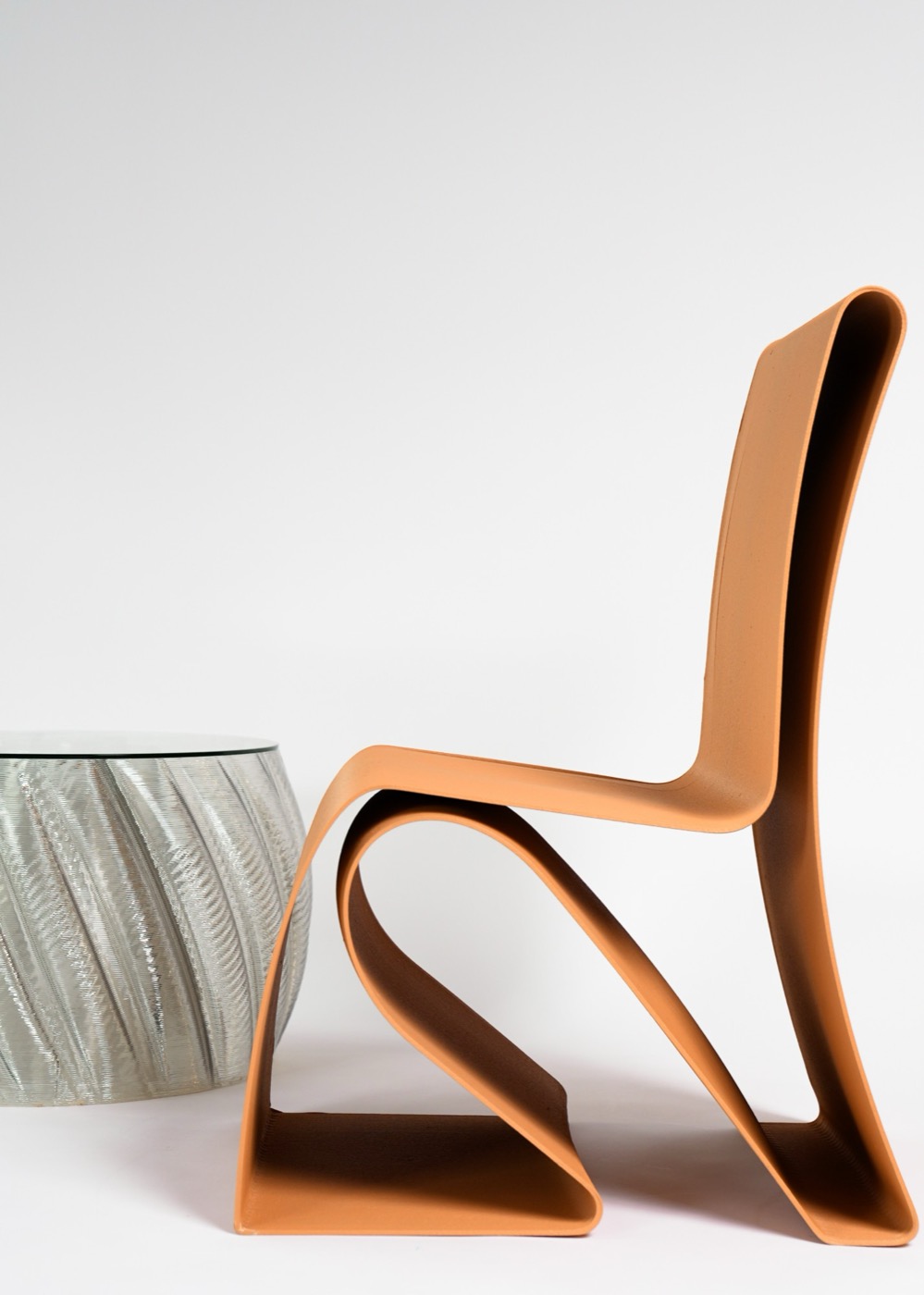 An orange printed ribbon chair beside a clear ribbed side table
