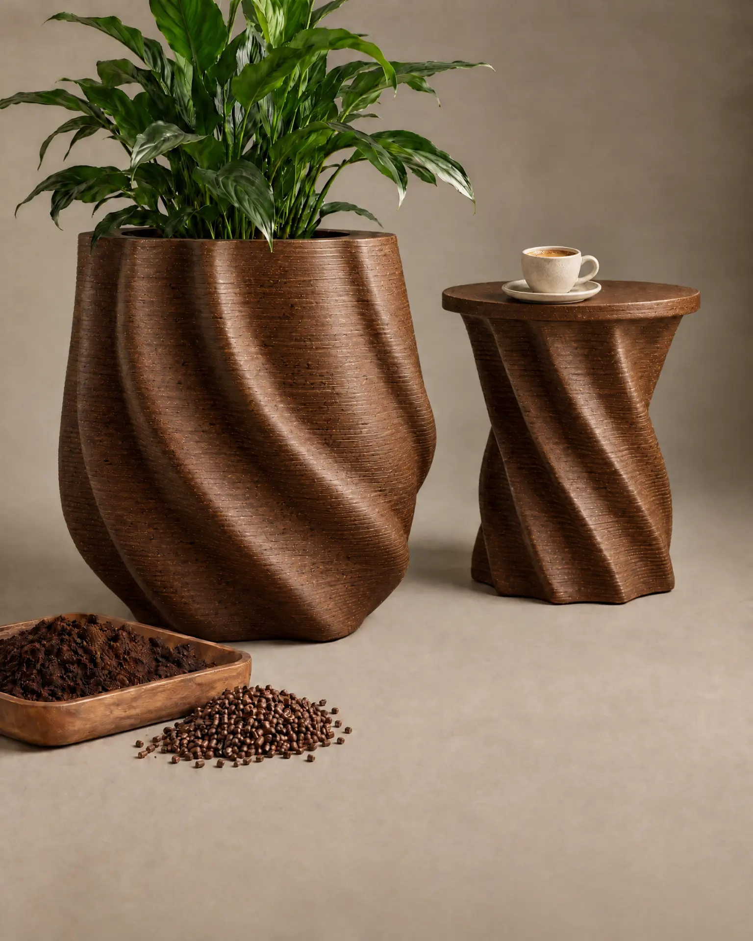 Twisted planter with a leafy plant and a matching spiral side table holding an espresso cup, both printed from a warm brown composite, beside a wooden tray of coffee grounds and pellets