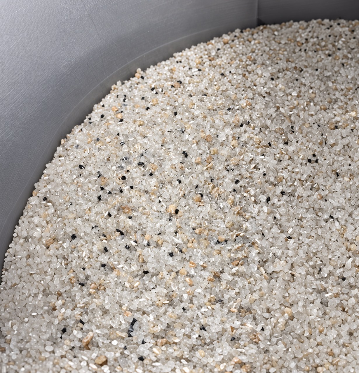Close-up of translucent white mineral aggregate with tan and black flecks held in a gray container