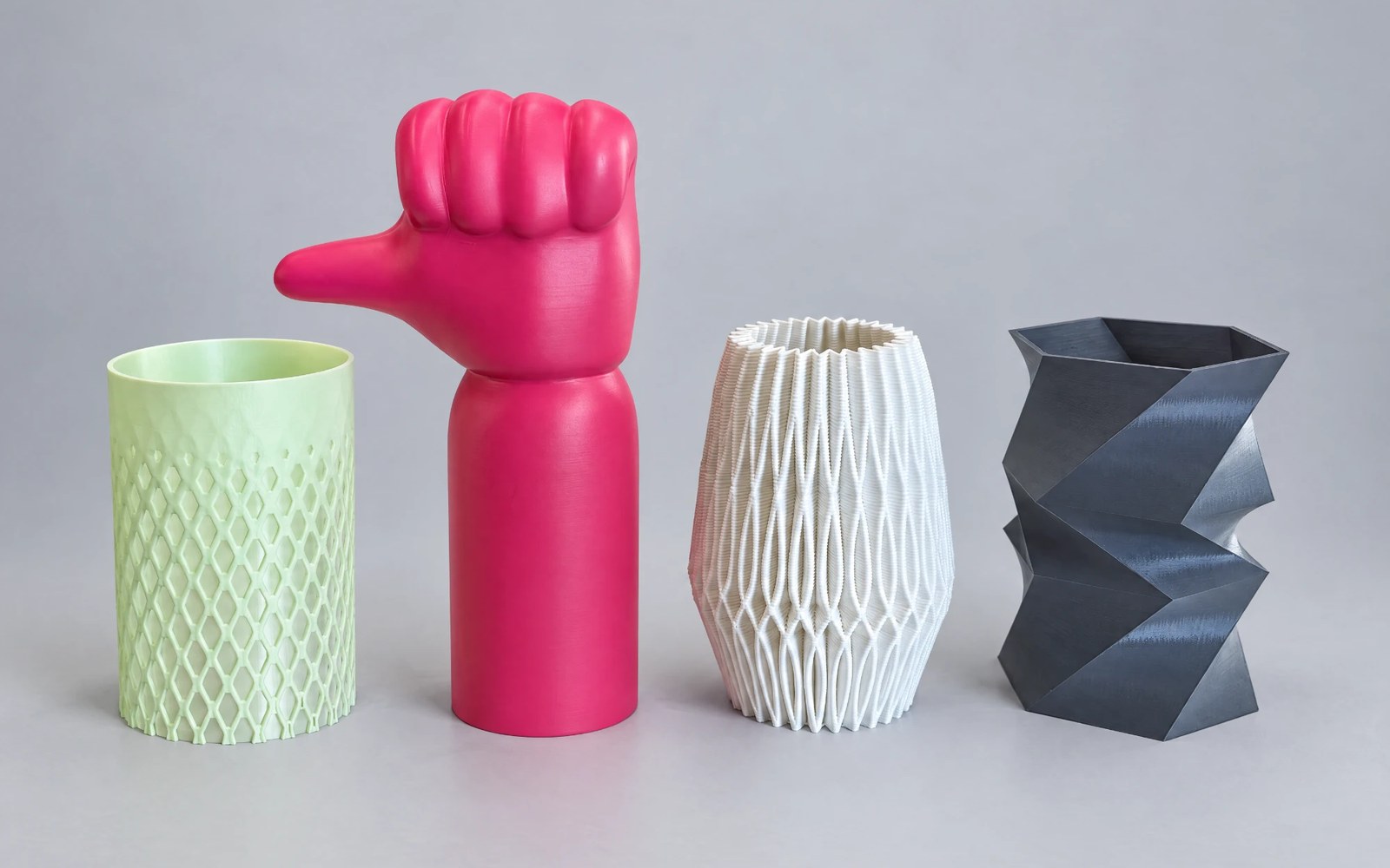 Four printed vases: a pale green lattice cup, a pink thumbs-up figure, a white ribbed vase and a charcoal faceted vase